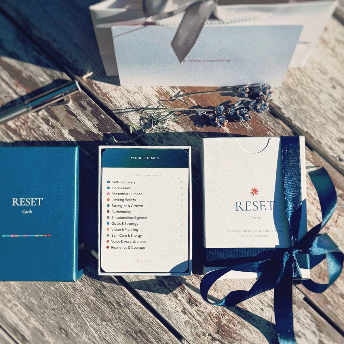 The RESET Cards box open beside its sleeve, tied with a navy ribbon, with an Aida Coaching gift bag behind