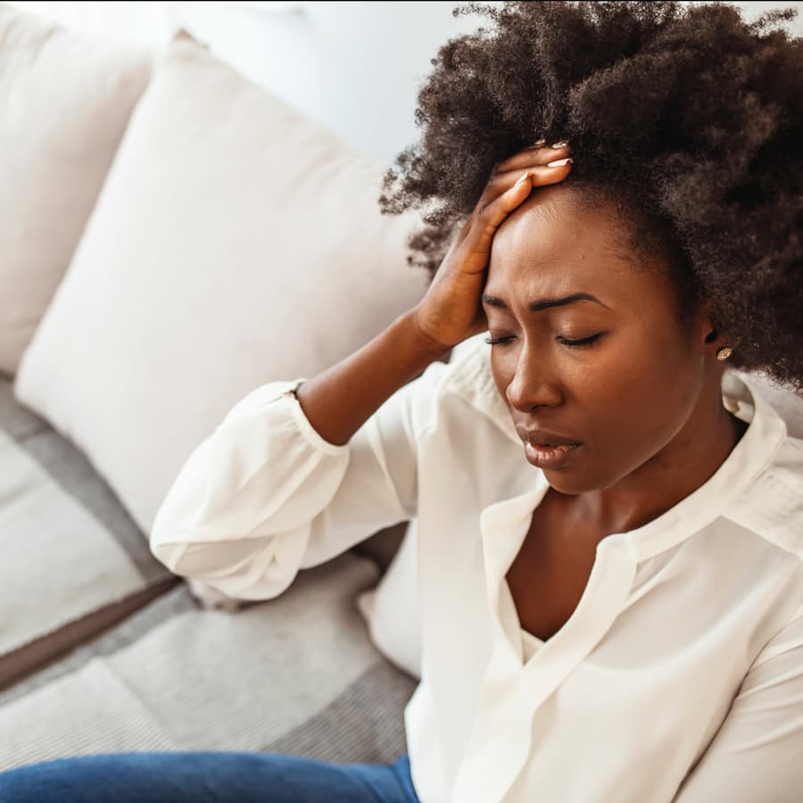 A woman sitting on a sofa with her hand to her forehead